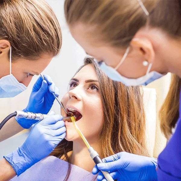 Dental professionals in gloves and masks examine patient's teeth with instruments in clinical setting
